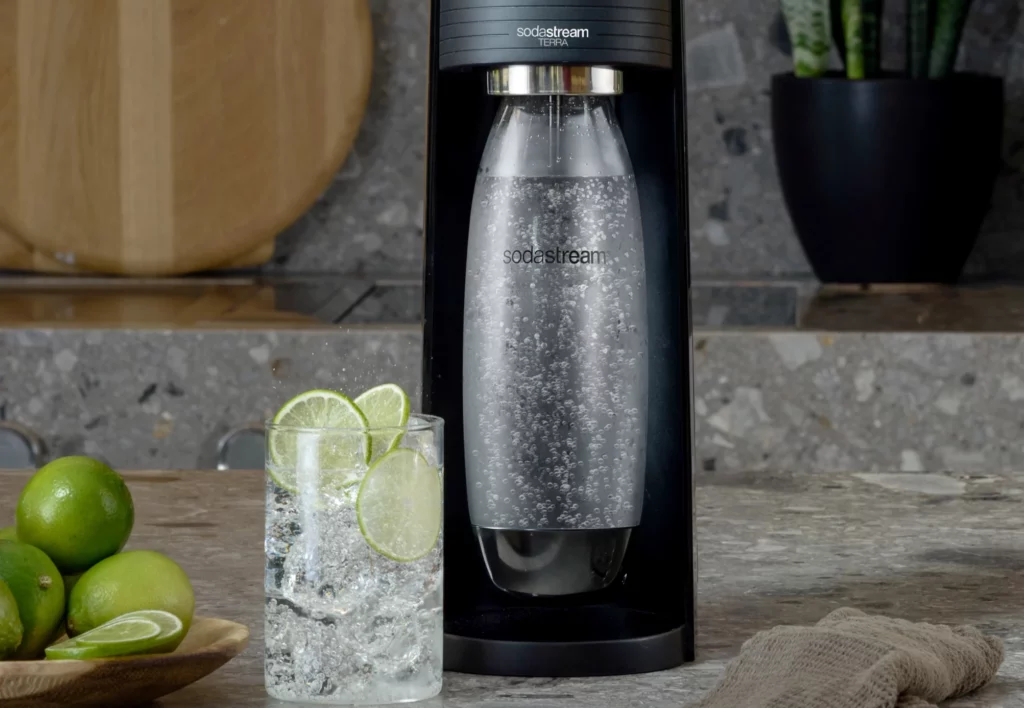 czarna maszyna terra firmy sodastream wraz z szklaną z napojem z dodatkiem limonki